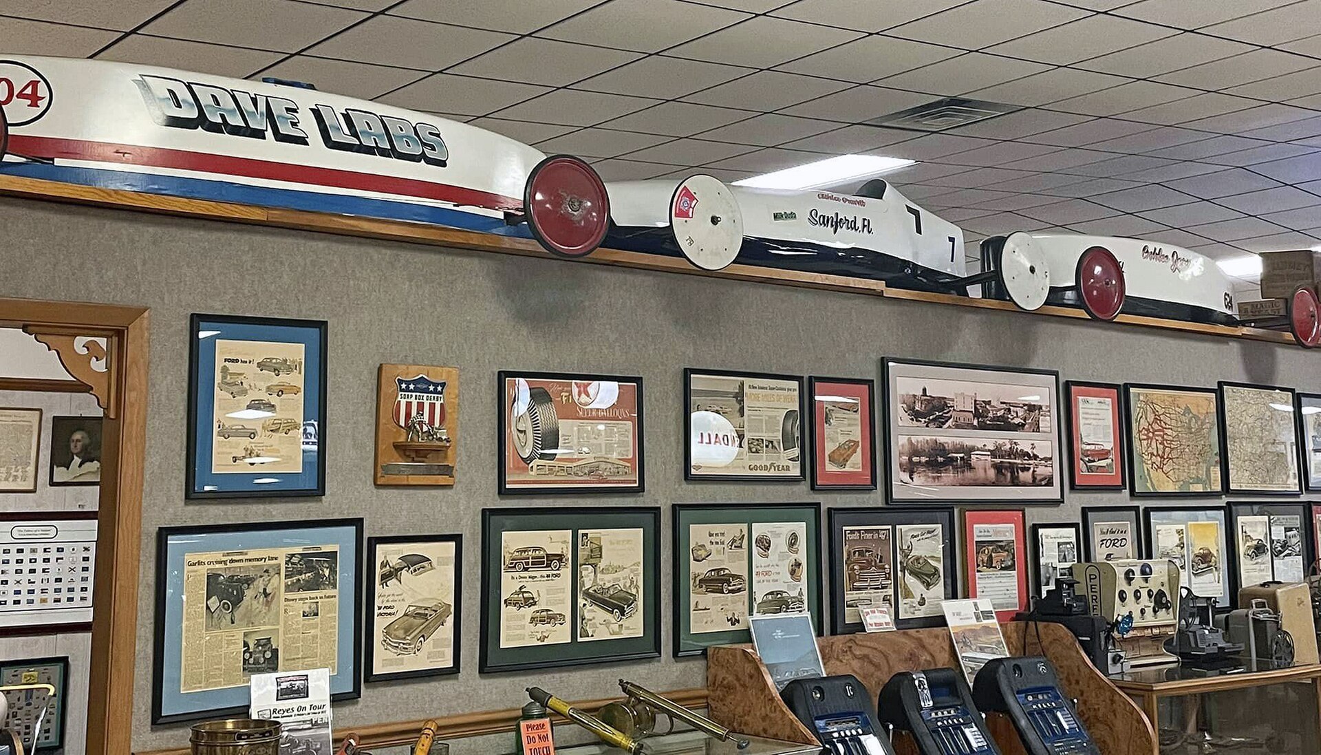 Three Soap Box Derby cars from the 1990s parked side by side on a museum floor under indoor lighting
