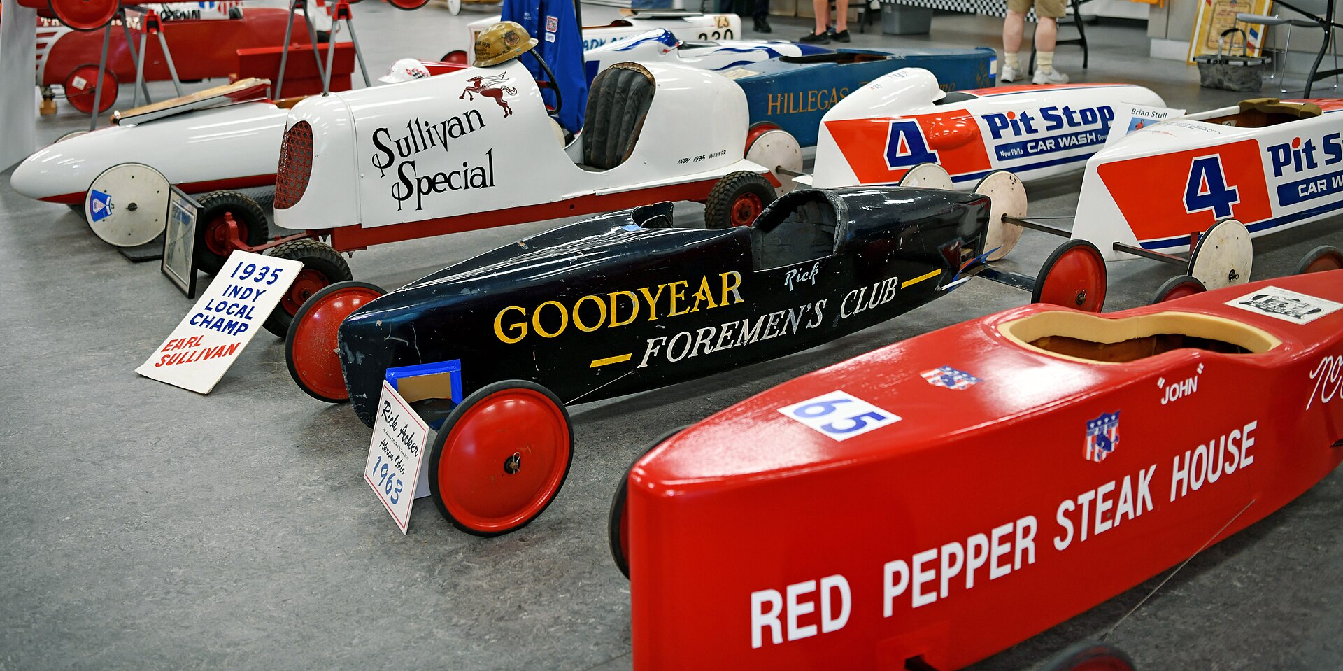 Colorful vintage Soap Box Derby cars from several decades displayed together at a 2022 car show in Akron